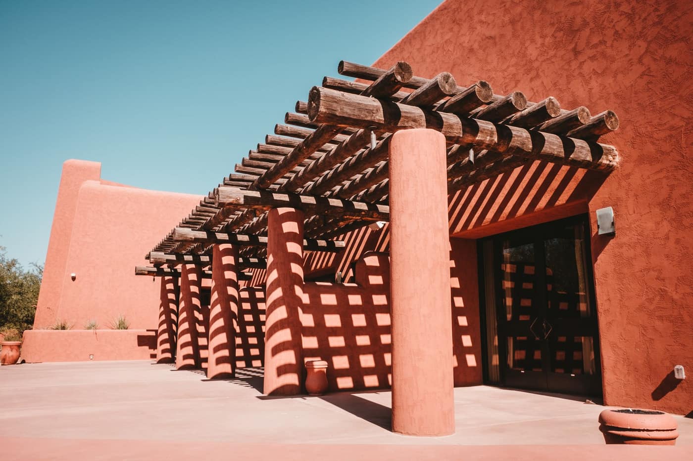 Terracotta adobe southwestern architecture with a timber pergola casting lattice shadows in Phoenix, Arizona